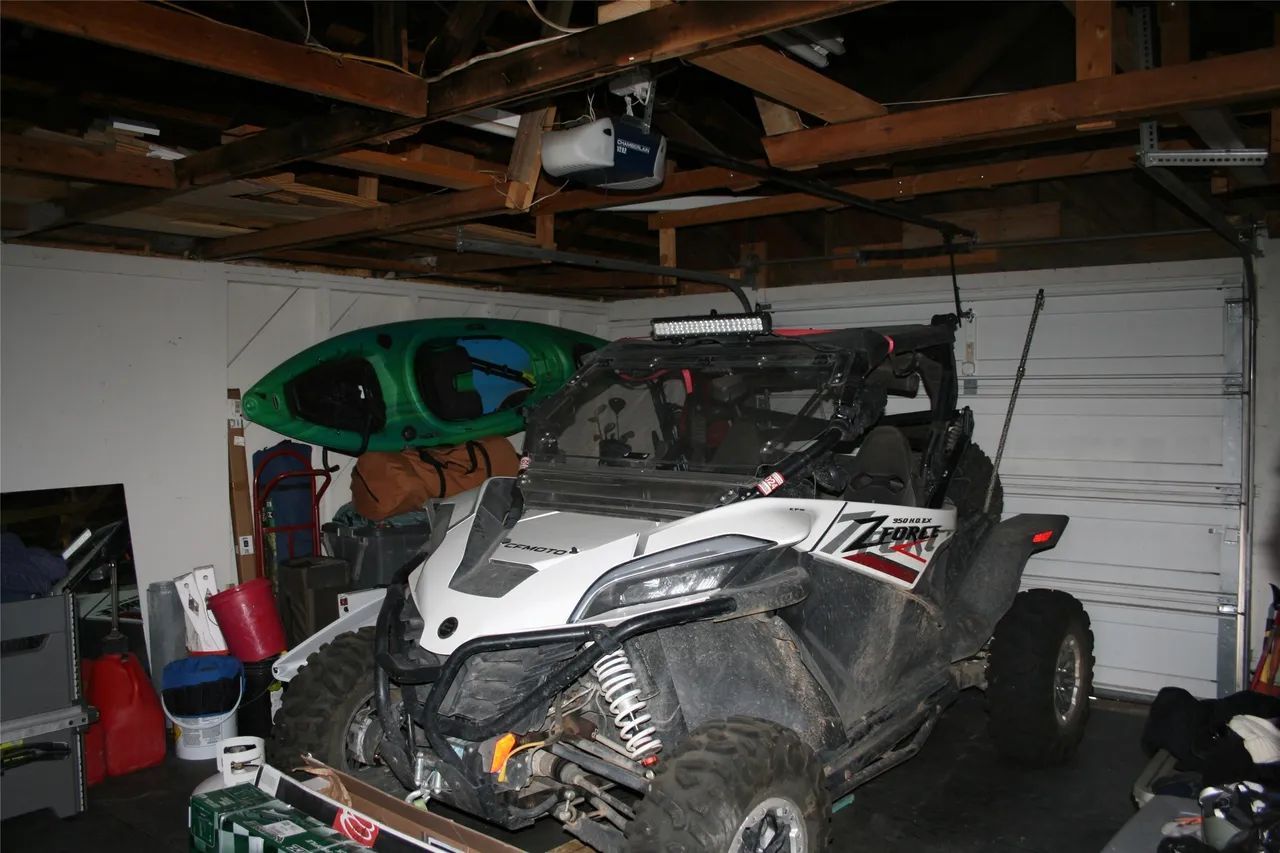 A white and black off-road utility vehicle parked in a dimly lit garage with a green kayak mounted on the wall behind it.