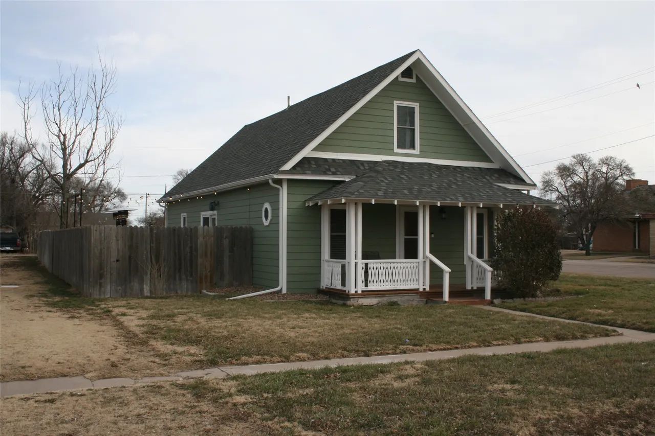 A gray, one-story house with a white-trimmed carport, a stone fire pit in the front yard, and scattered landscaping.