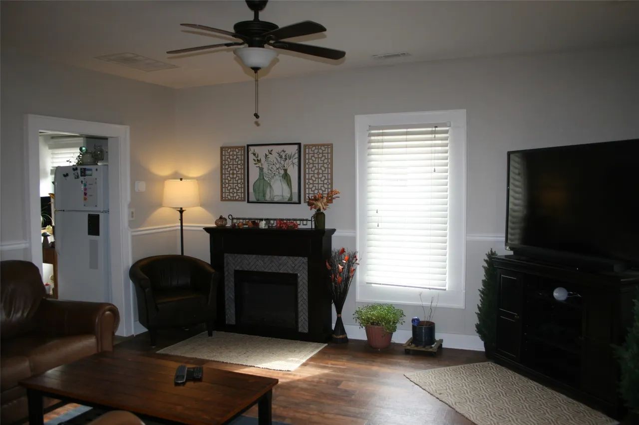 A living room with a fireplace, television, wooden coffee table, armchair, and brown sofa on hardwood floors.
