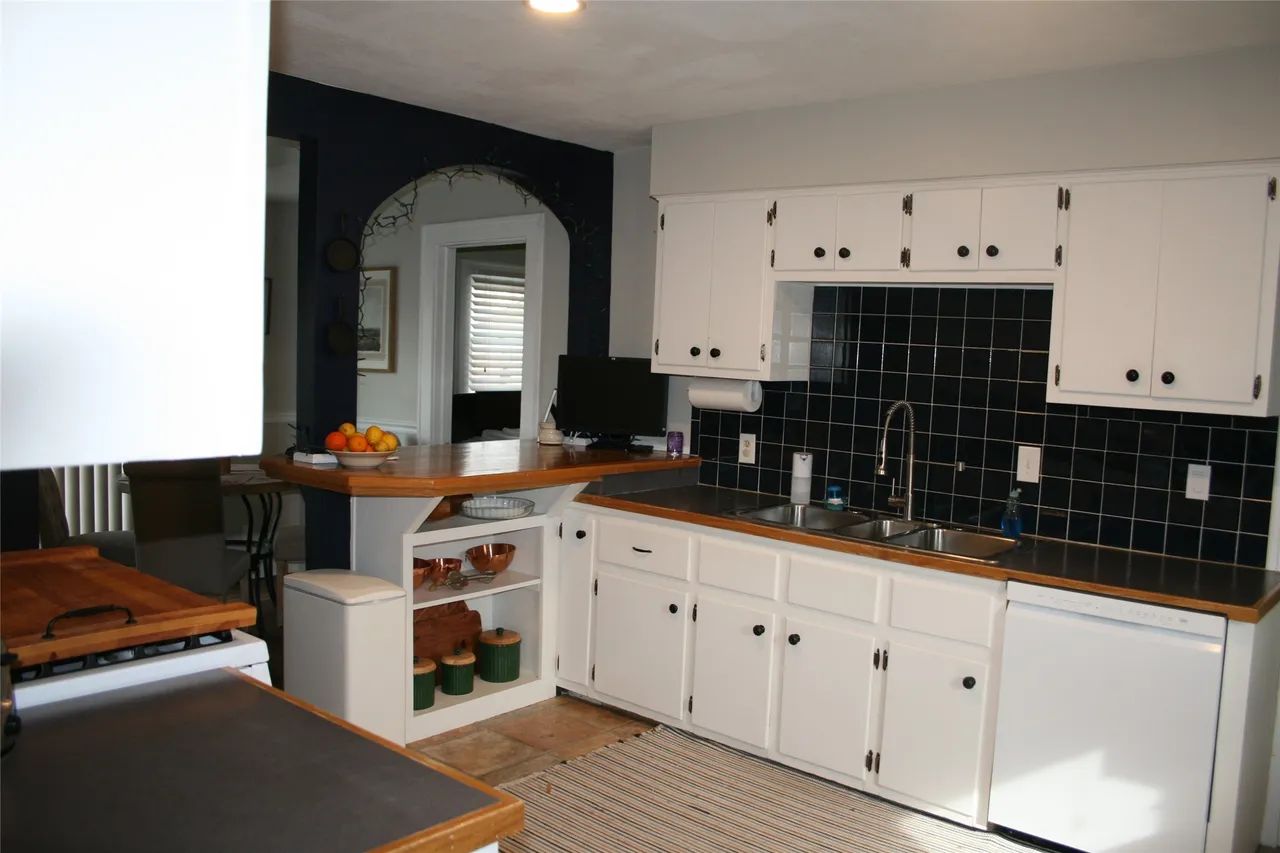 Kitchen with white cabinets, dark tile backsplash, wooden countertops, and a breakfast bar in an arched entryway.