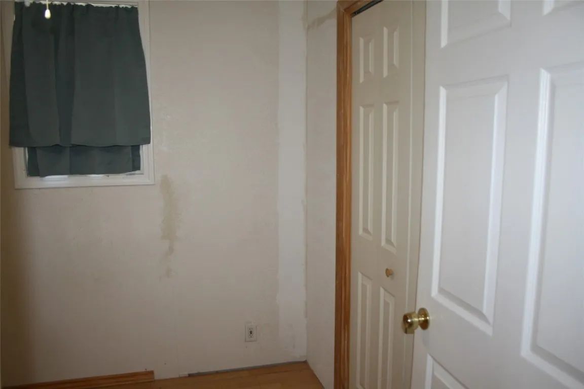 A room corner with light-colored walls, a window covered by a grey curtain, and a white interior door.