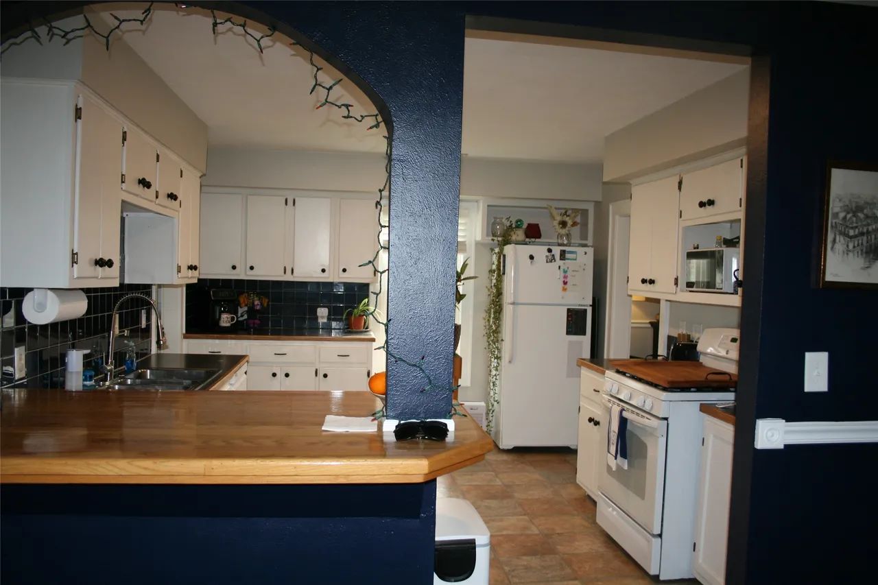 A kitchen featuring white cabinets, wood countertops, and a dark blue arched wall opening between rooms.