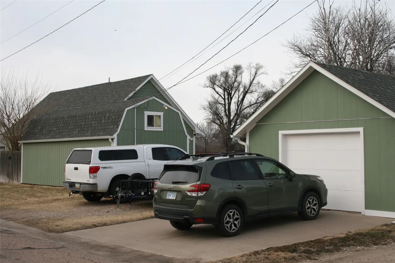 A white pickup truck and an olive green SUV parked in front of two green storage buildings with white trim.