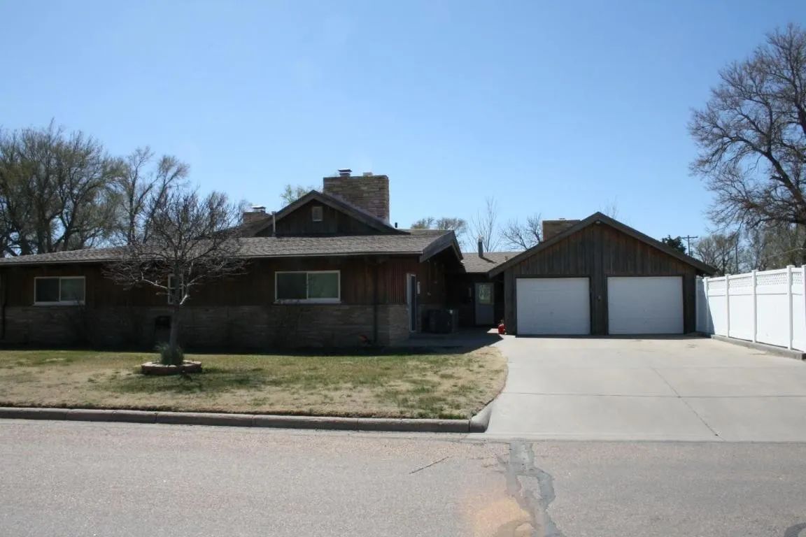 Single-story brown home with a stone lower exterior, a two-car garage, and a white privacy fence on a suburban street.