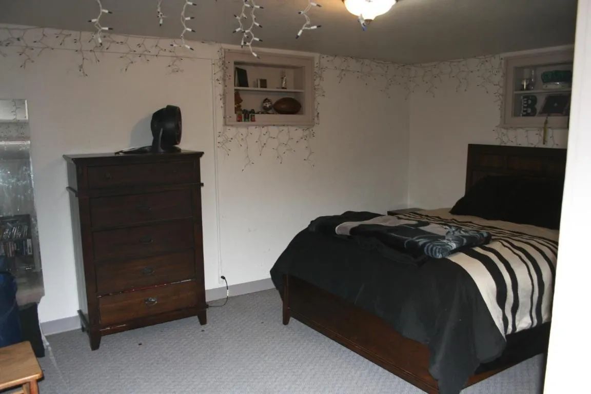 A bedroom with a dark wood dresser and bed featuring a black and white striped comforter, illuminated by string lights.