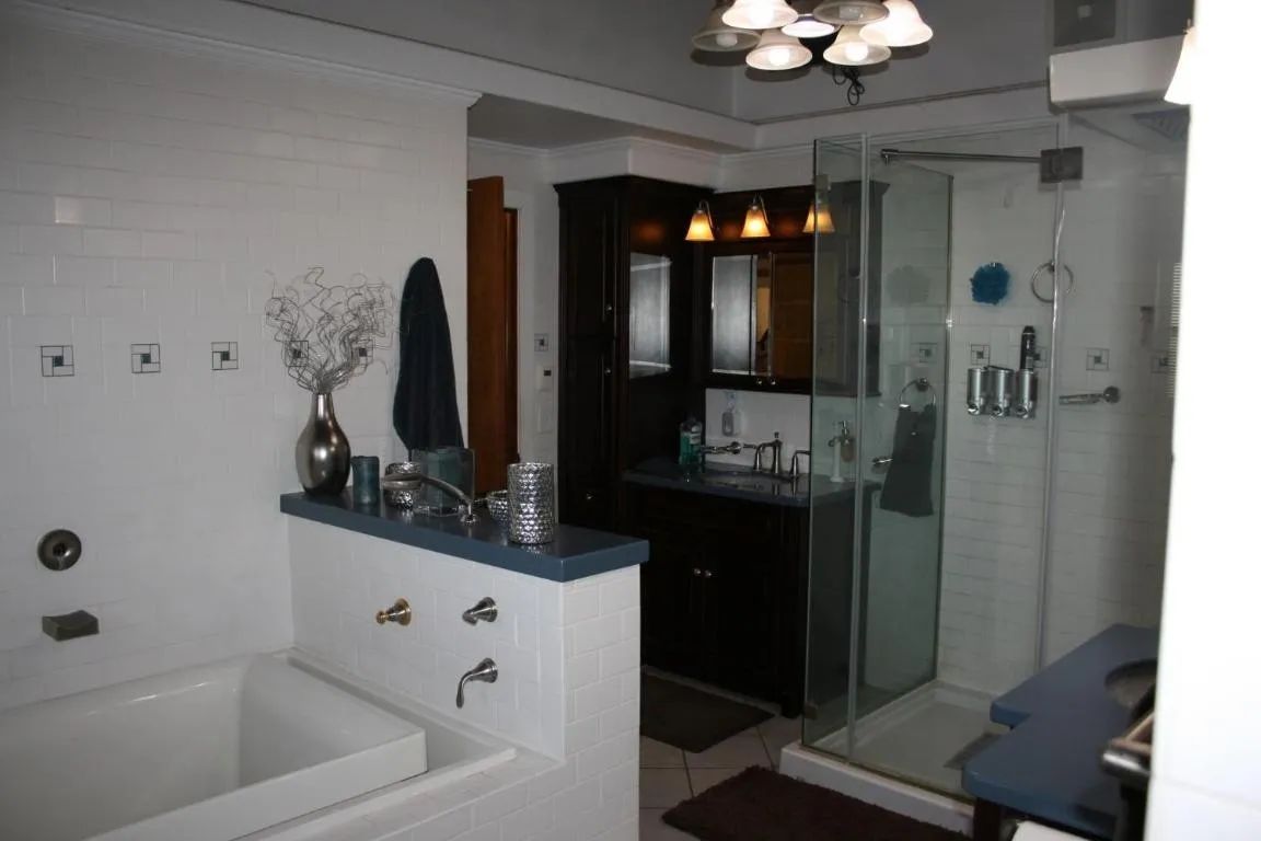 A modern bathroom featuring a white soaking tub, a dark wood vanity, and a glass-enclosed shower against white tiled walls.