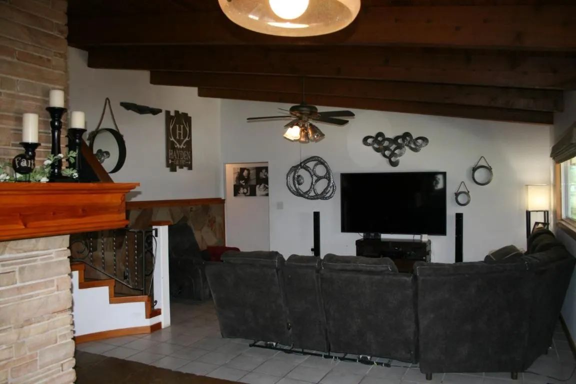 Living room featuring a dark gray sectional sofa, a wall-mounted TV, vaulted wood-beam ceilings, and stone accents.