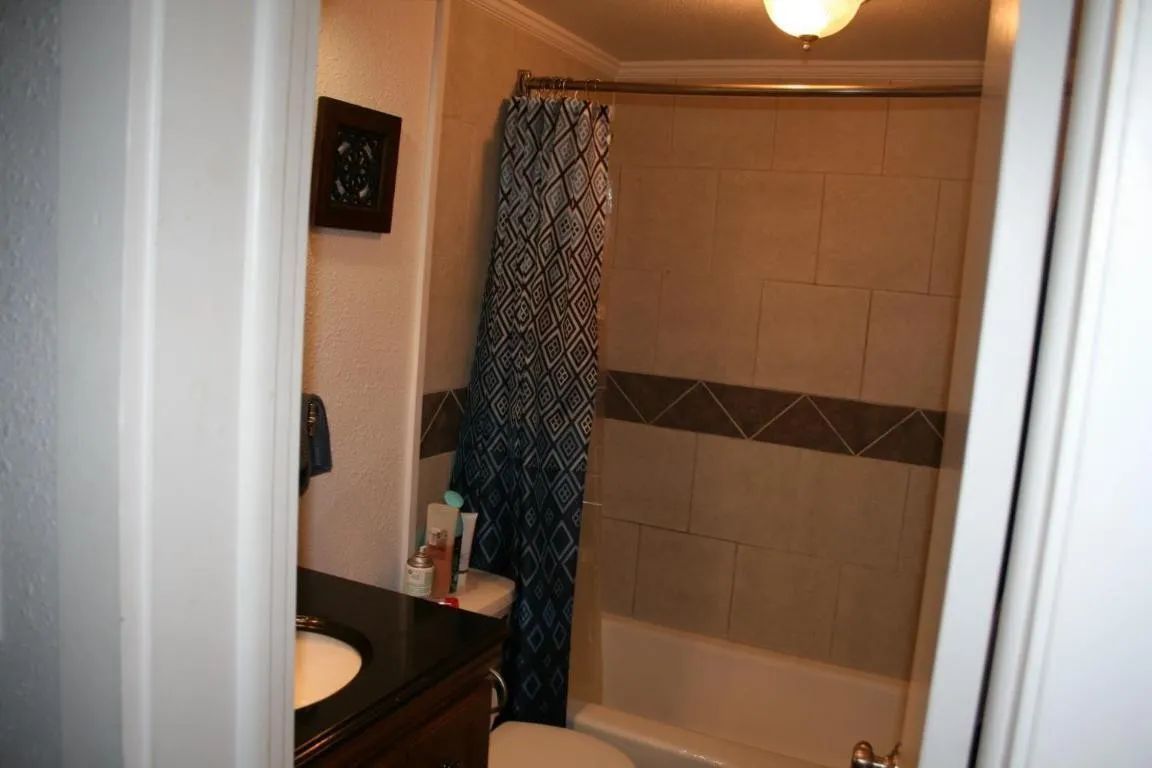 A bathroom featuring a shower with a dark blue and white patterned curtain, tan tiled walls, and a black vanity.
