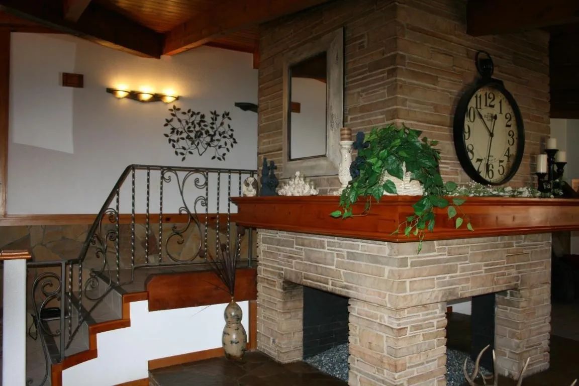 A stone fireplace with a wooden mantel sits beside a decorative metal staircase railing in a rustic home interior.