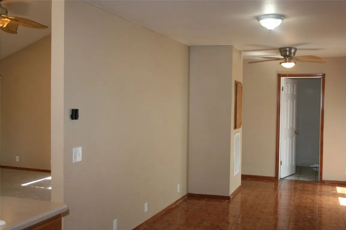 An interior view of a room with beige walls, hardwood flooring, two ceiling fans, and an open doorway leading to a room.