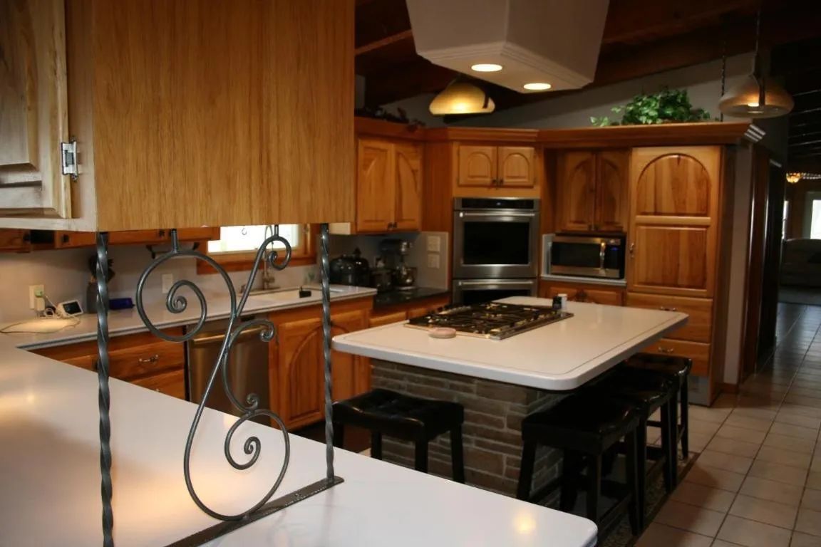 A kitchen with wooden cabinets, a central island featuring a stovetop and bar seating, and a decorative wrought iron piece.