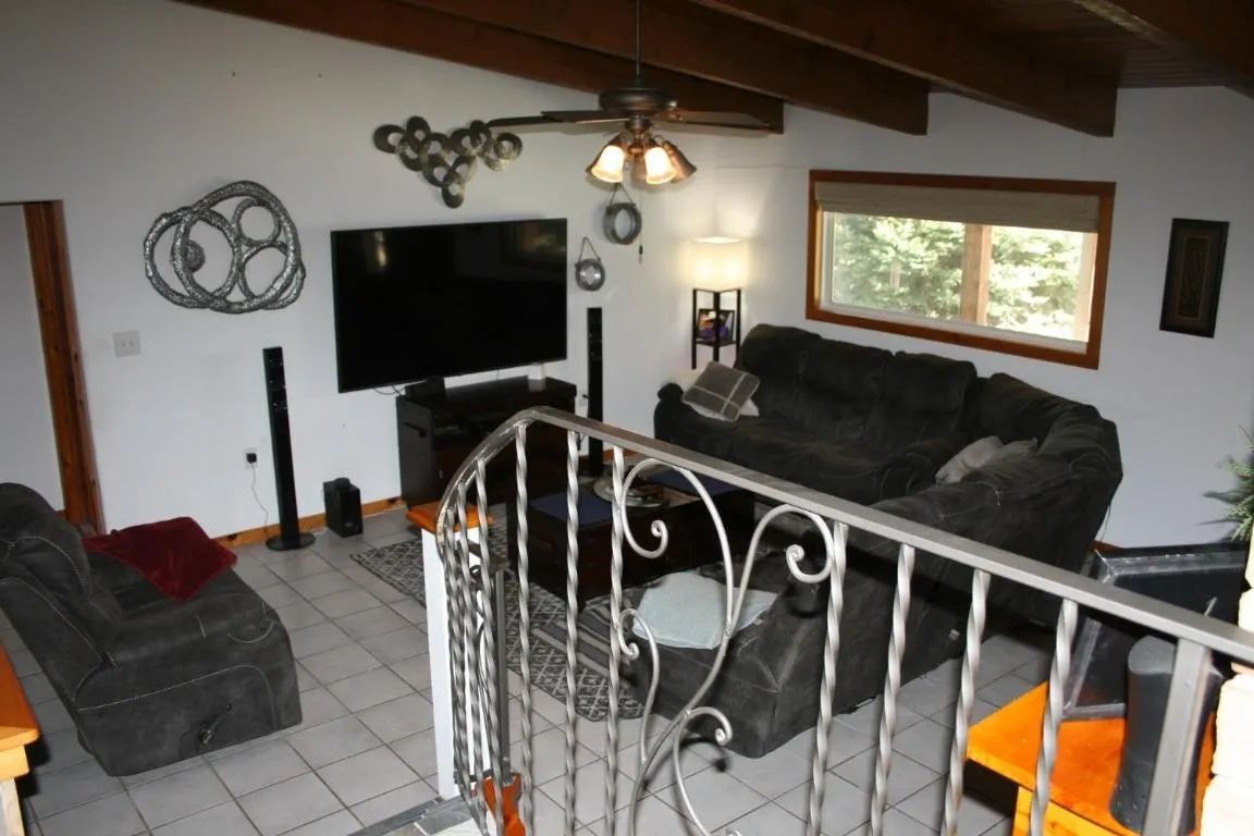 A high-angle view of a living room with grey sofas, a large television, a ceiling fan, and a wrought iron stair railing.
