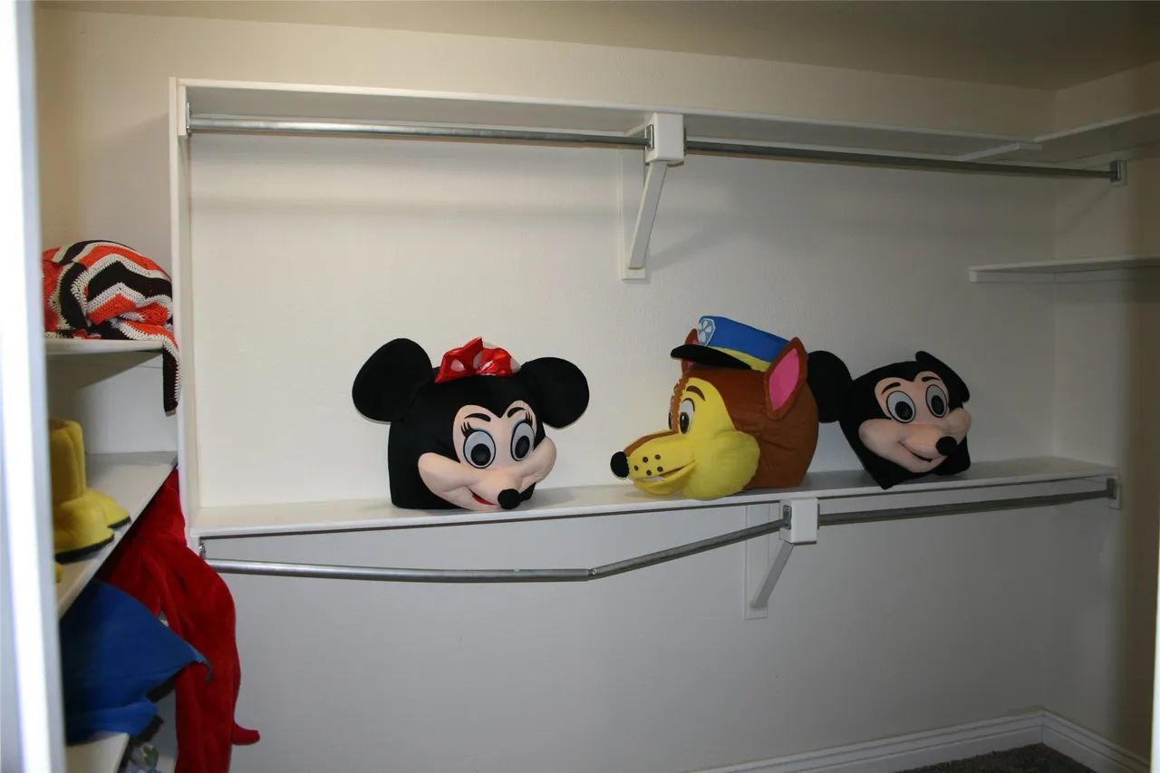 Three character mascot heads—Minnie Mouse, a police dog, and Mickey Mouse—sit on a white closet shelf.