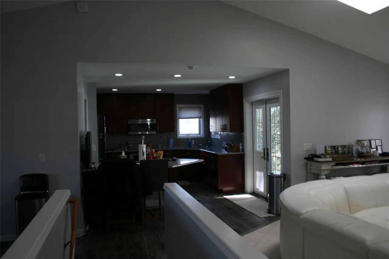 A view from a loft into a kitchen with dark wooden cabinets, a white couch in the foreground, and a glass-paneled door.