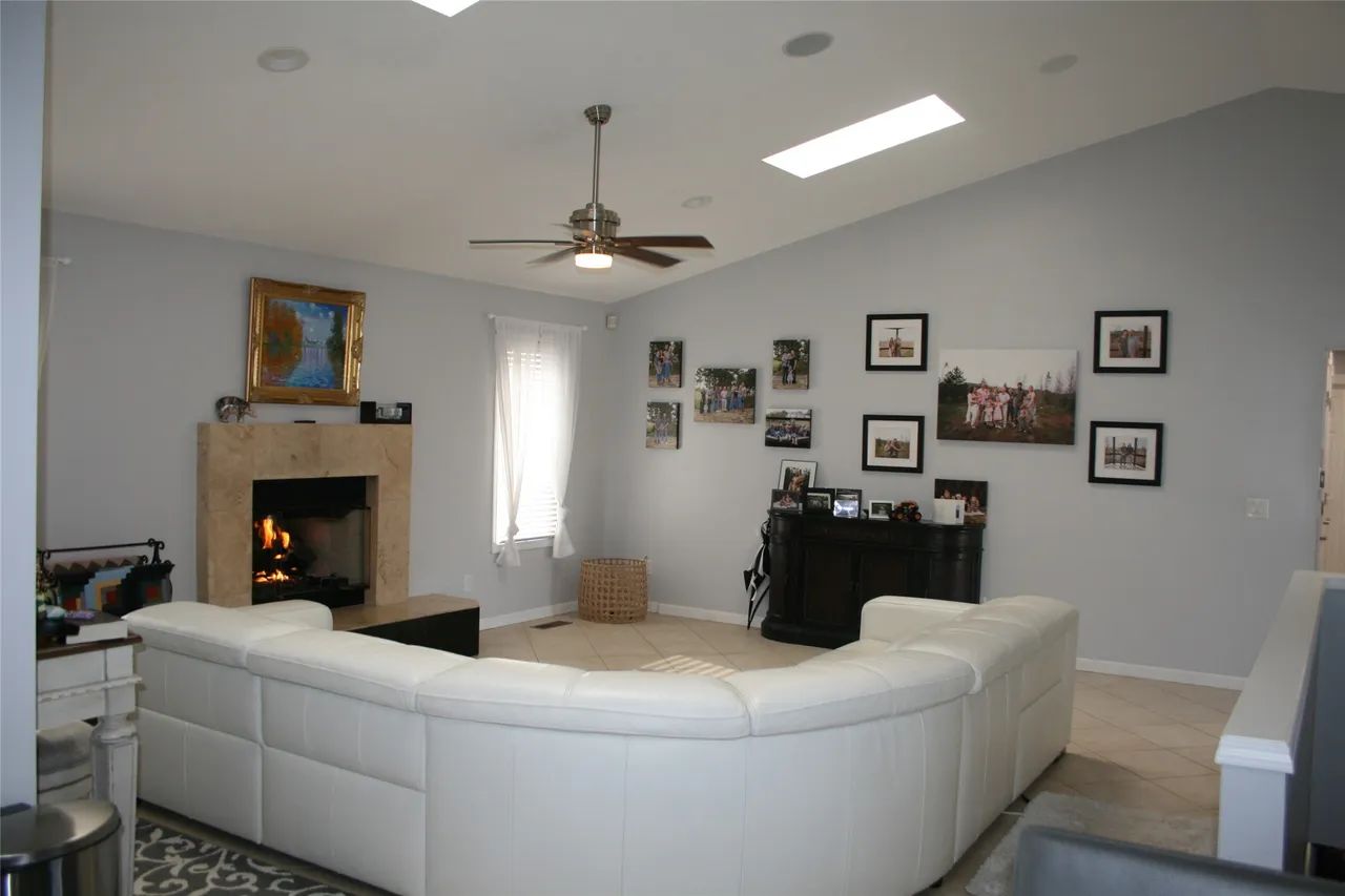A living room with a lit fireplace, white sectional sofa, ceiling fan, and a gallery wall with framed pictures.
