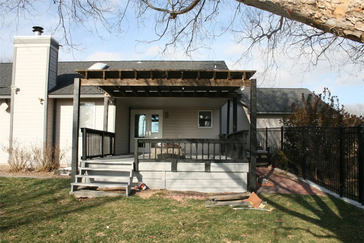 A residential backyard deck featuring a wooden pergola, gray stairs, and a black railing, set against a house exterior.