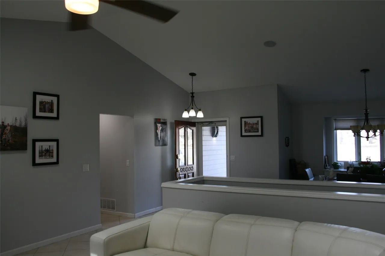 A gray-walled living room features a white sofa in the foreground, two framed pictures on the wall, and a view of a doorway.