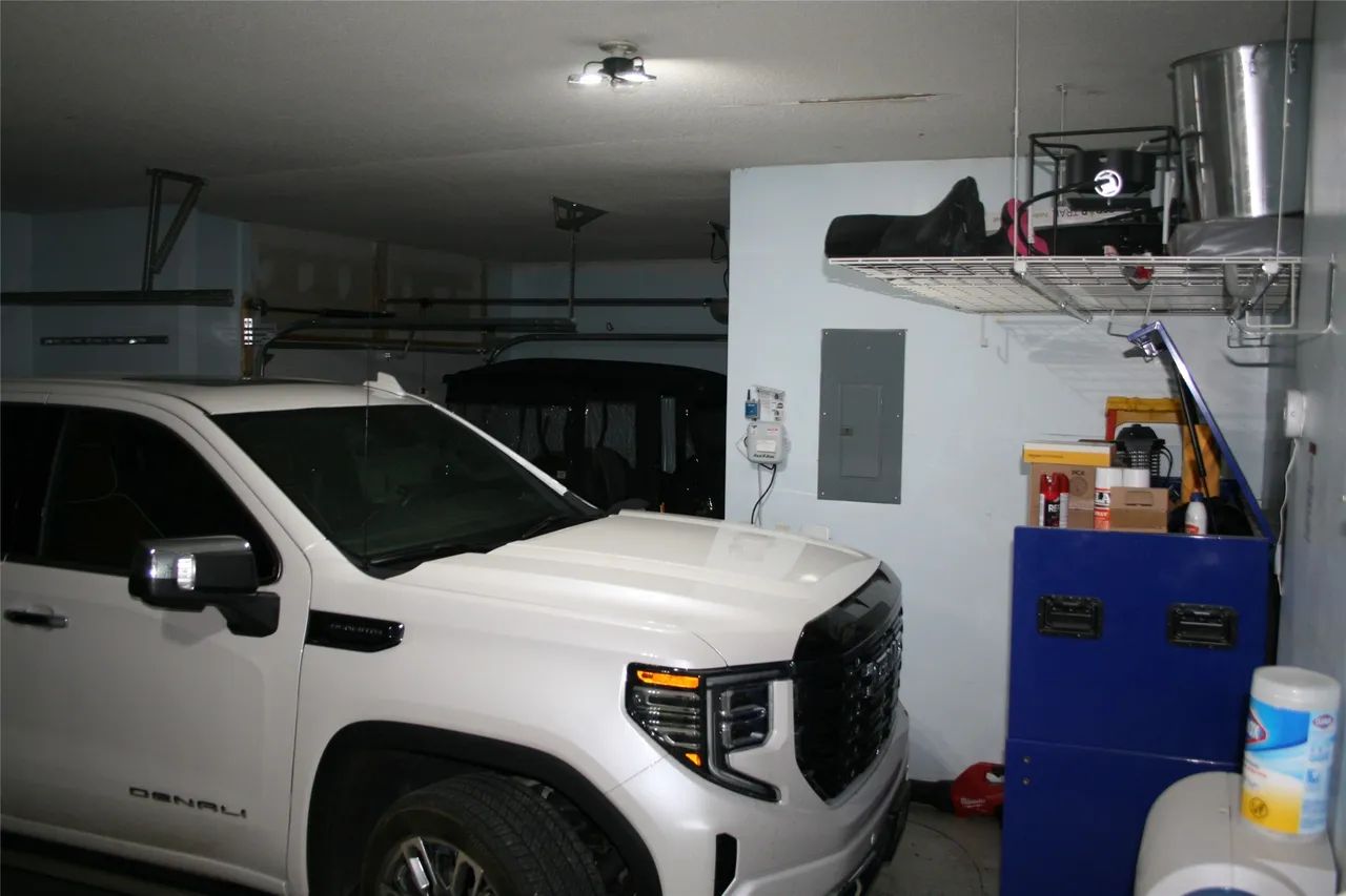 A white truck parked inside a home garage, featuring an overhead storage rack, a blue tool cabinet, and a wall panel.