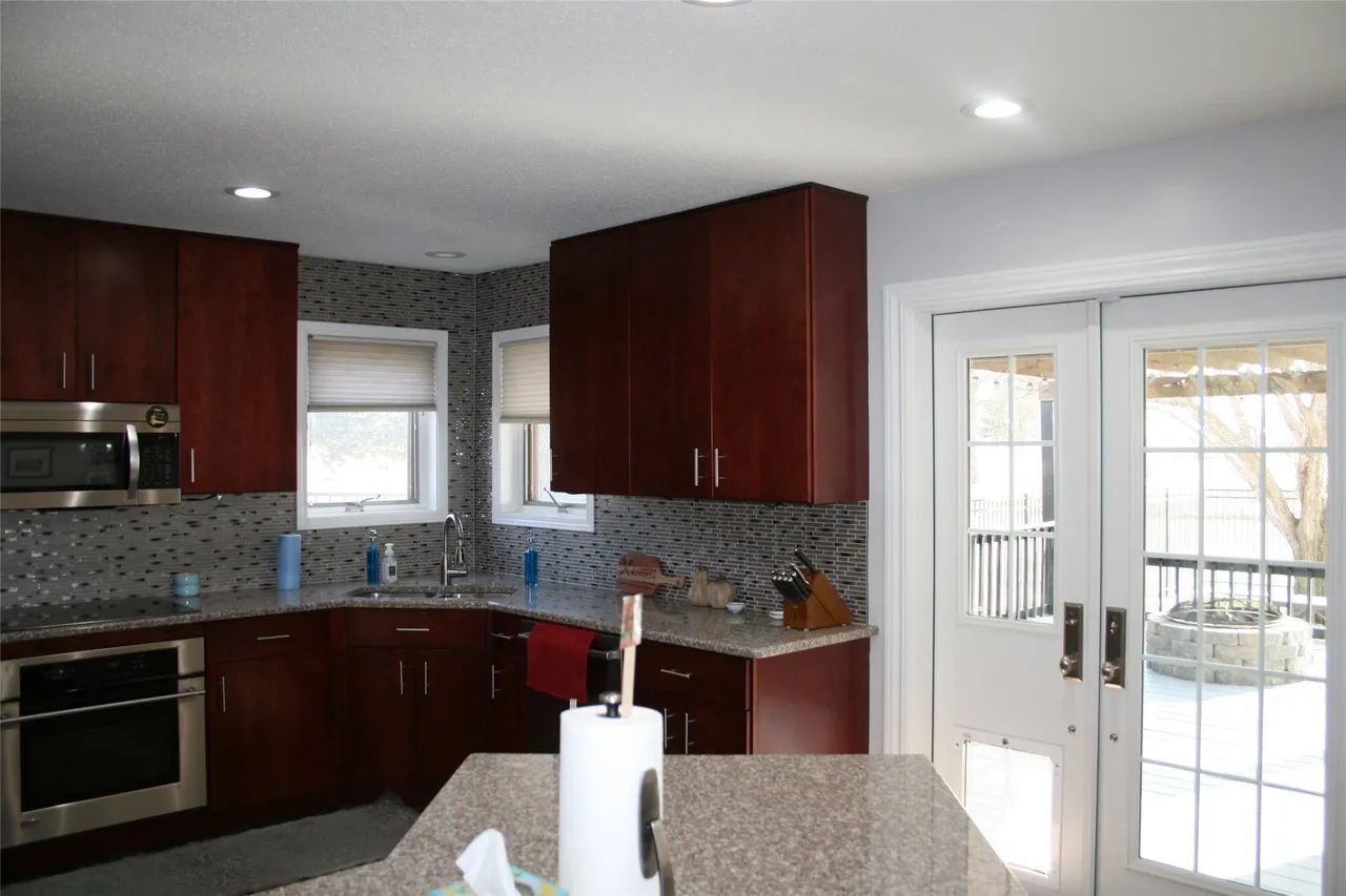 A kitchen featuring dark wood cabinets, granite countertops, a tiled backsplash, and glass-paned doors leading outside.