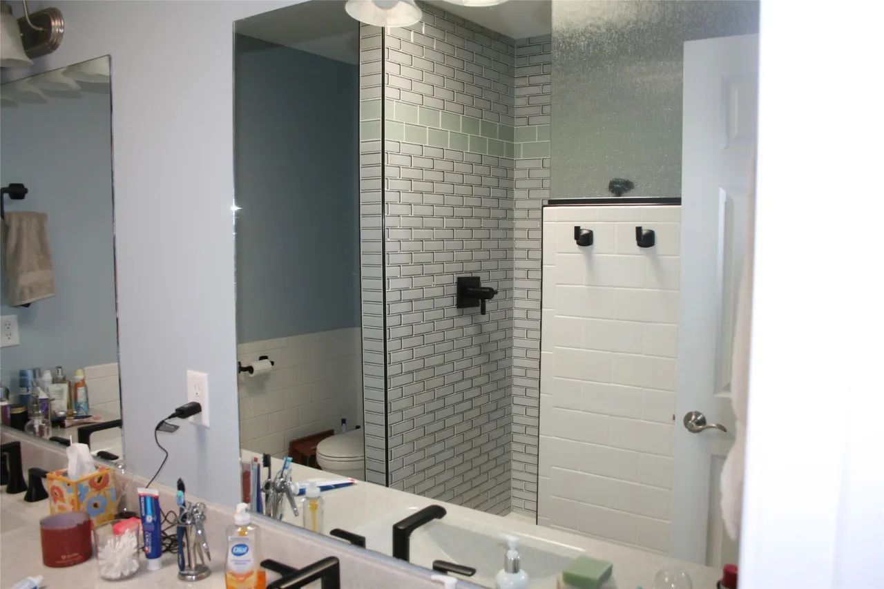 A bathroom vanity with a mirror reflecting a shower area tiled with white bricks and black fixtures.