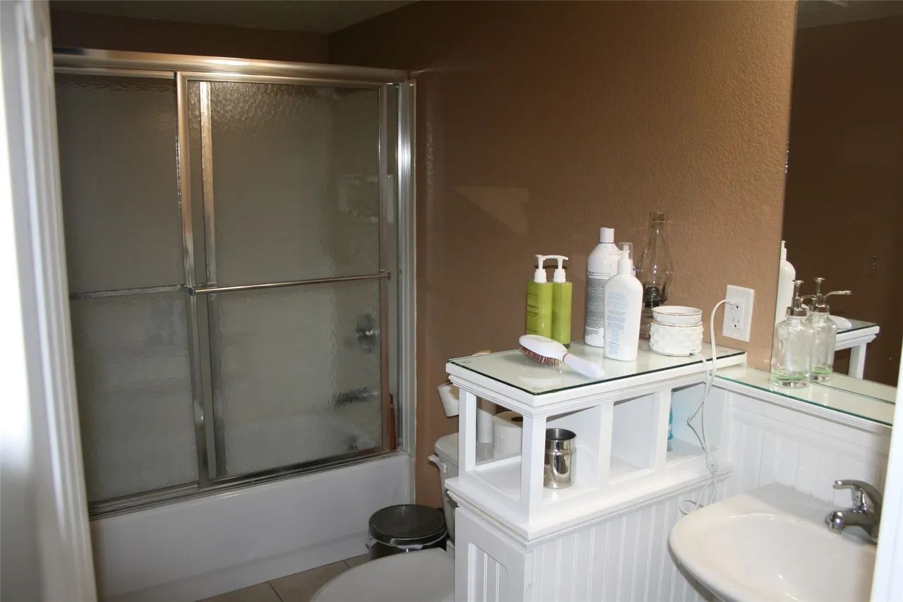 A bathroom with a sliding-door shower stall next to a white vanity unit and sink against brown walls.
