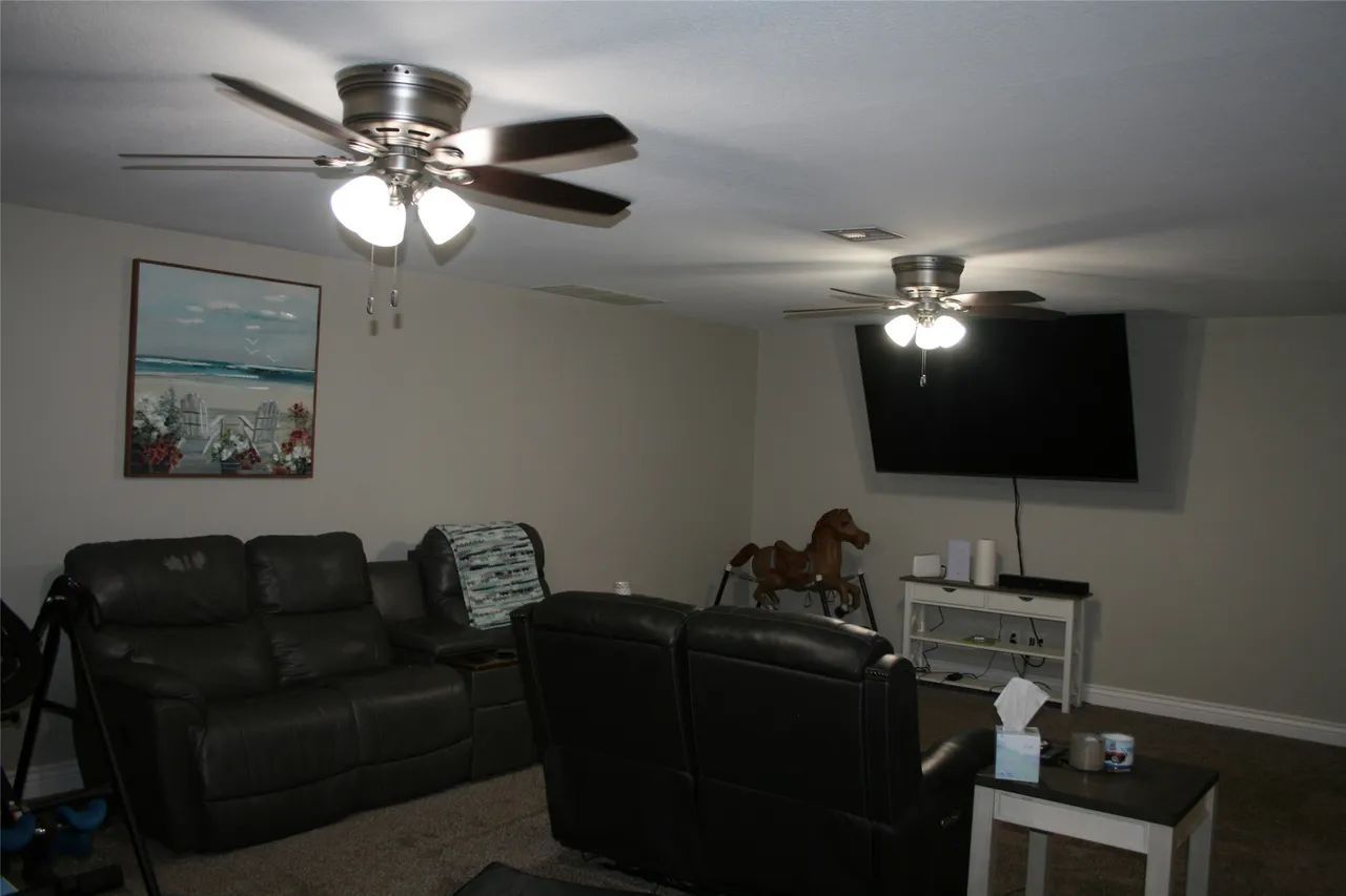 A living room with two dark leather sofas, a mounted flat-screen TV, a toy horse, and two ceiling fans.