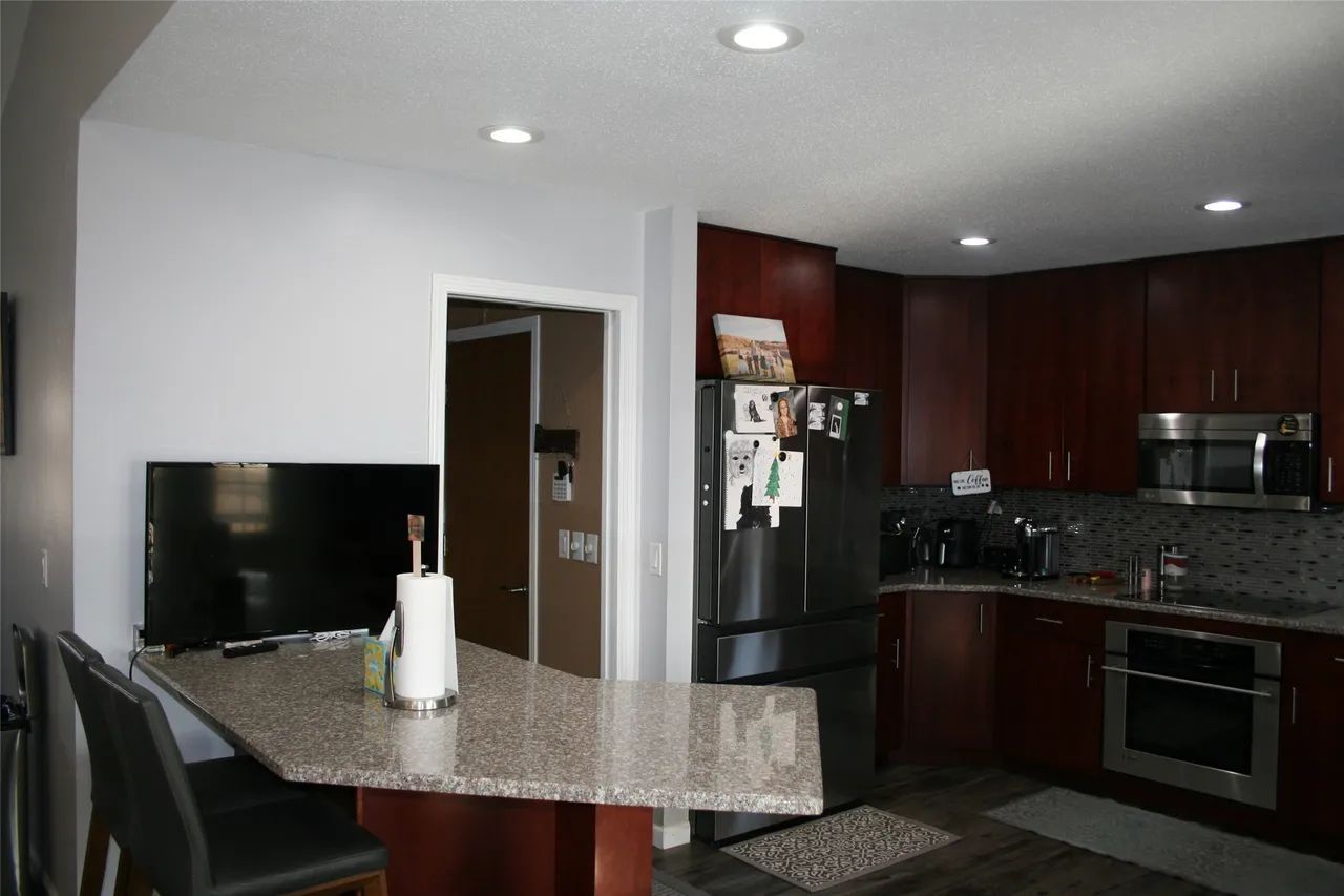 A kitchen with dark wood cabinets, stainless steel appliances, and a granite-topped peninsula with chairs.