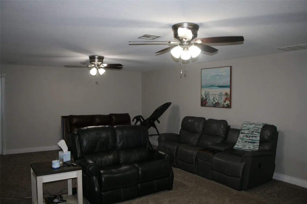 Living room with two dark leather sofas, a side table, ceiling fans, and framed wall art.