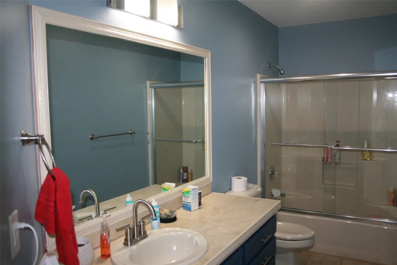 A bathroom with blue walls, a large white-framed mirror over a vanity sink, and a shower with a sliding glass door.