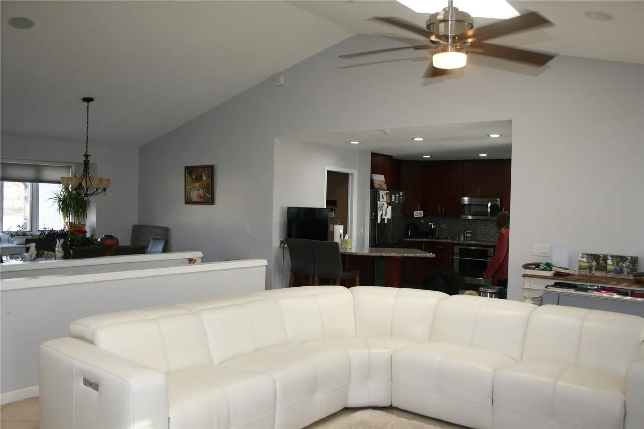 A large white sectional sofa sits in a living room with vaulted ceilings, a ceiling fan, and an adjacent kitchen area.