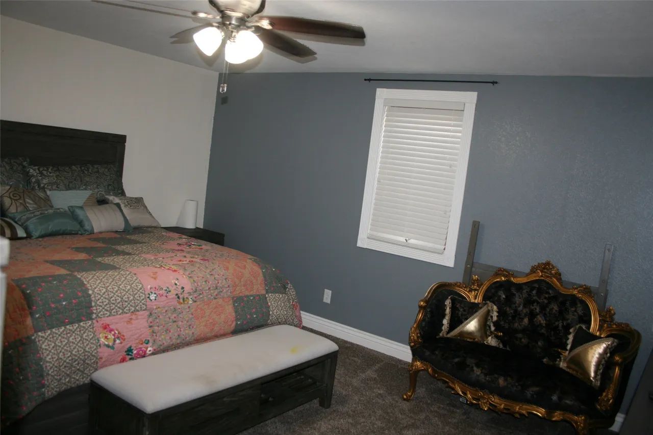 A bedroom with a patterned quilt on a bed, a gray accent wall with a window, and a vintage-style black velvet sofa.