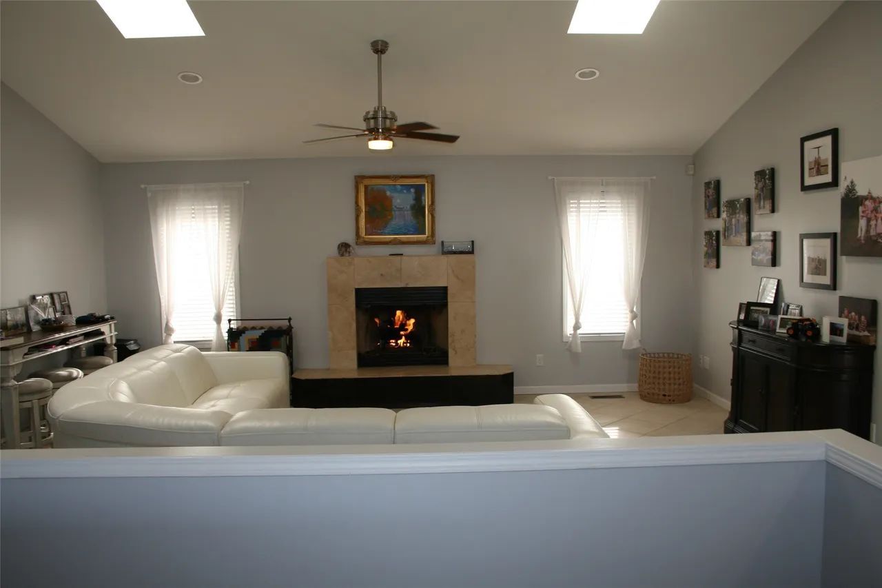 Living room with a white sectional sofa, fireplace, ceiling fan, and framed wall art in a neutrally decorated home.