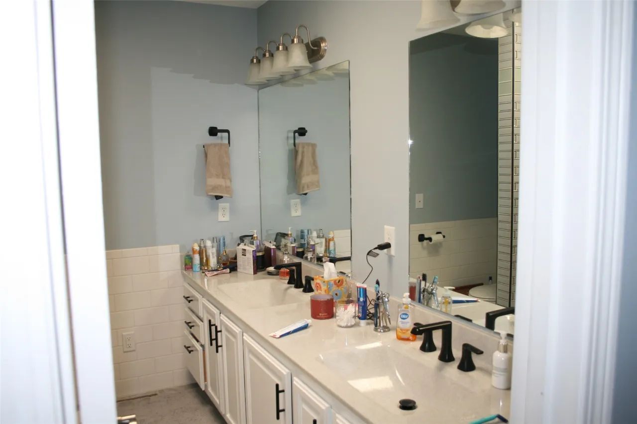 A double-sink bathroom vanity with white cabinets, a light-colored countertop, mirrors, and blue walls.