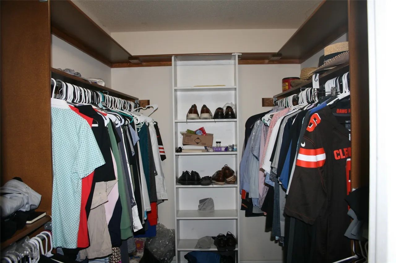 A walk-in closet with clothes hung on both sides and a central shelving unit containing shoes and small items.