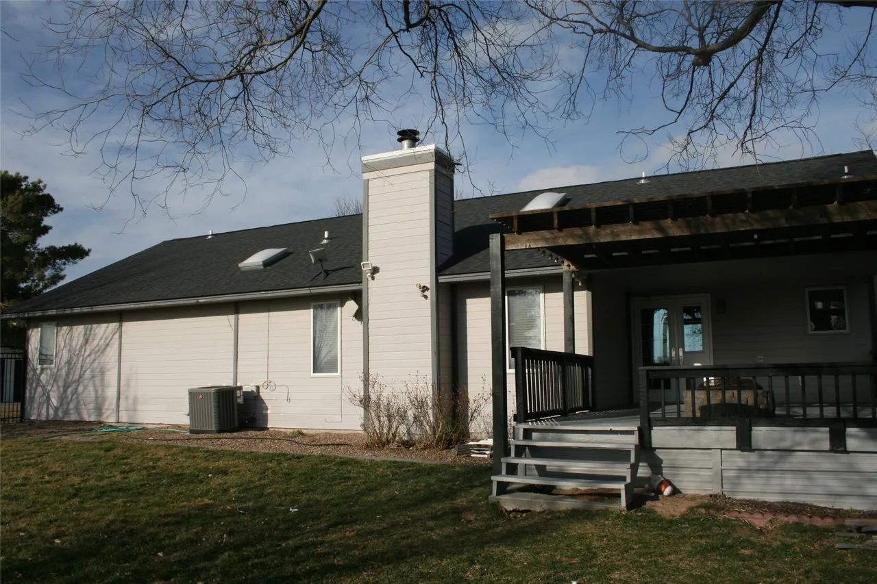 Backyard view of a beige house with a brick chimney, a dark roof, skylights, and a wooden deck with a pergola.