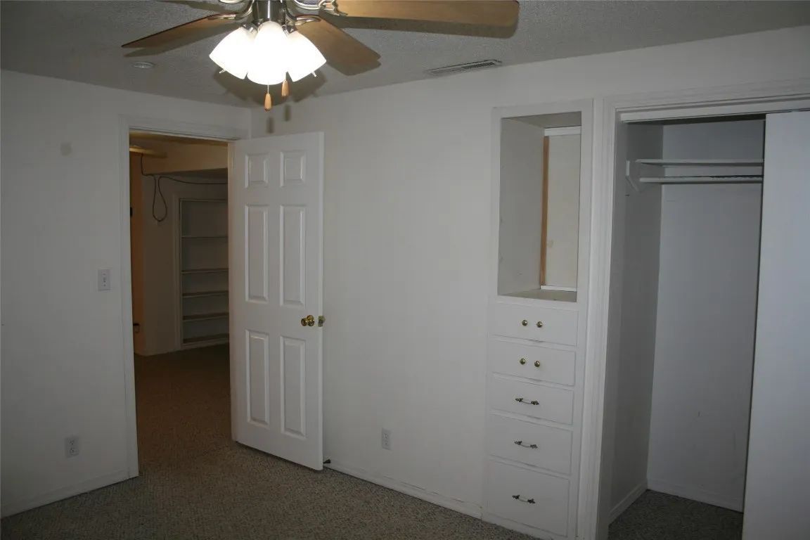 An interior view of a room with a white door, built-in wooden drawers, a closet, and a ceiling fan.