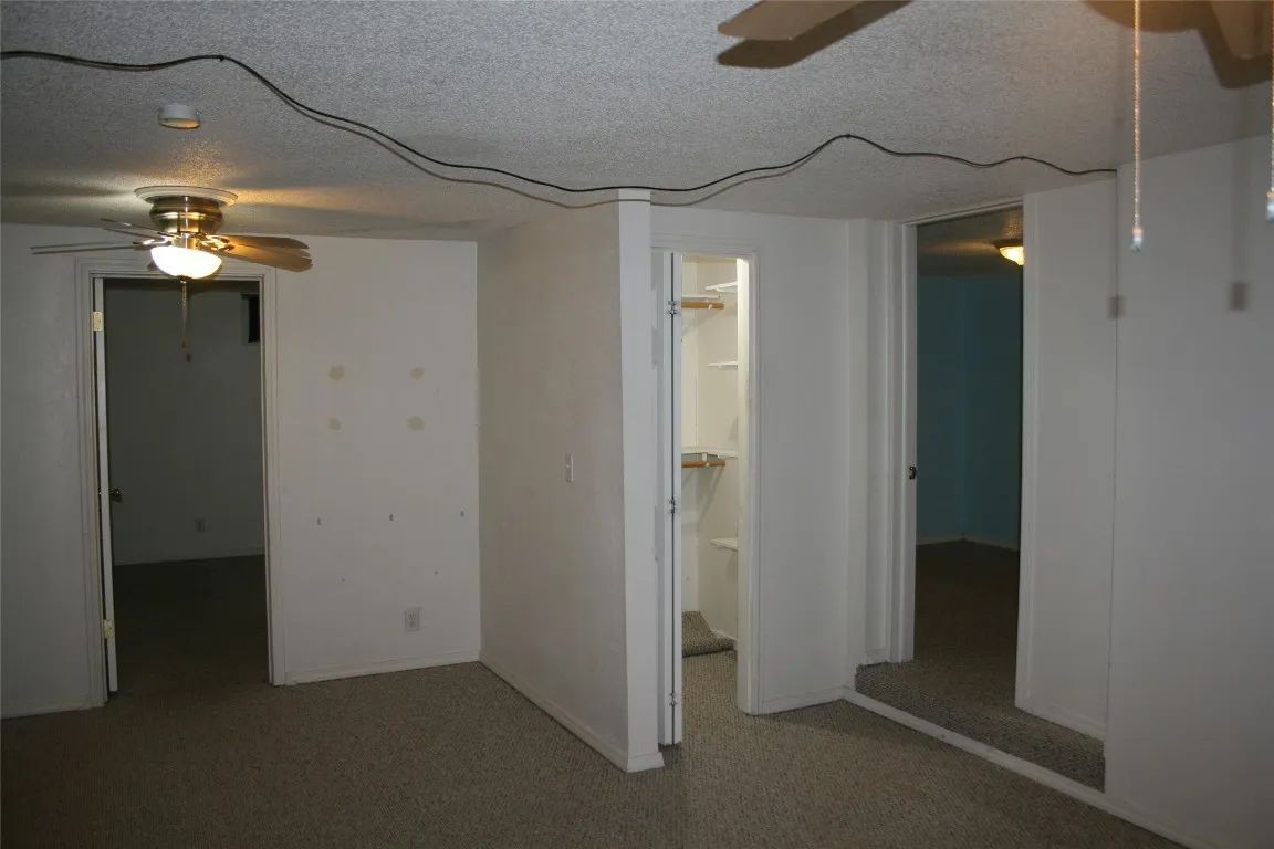 An interior view of a room with carpeted floors, white walls, two doorways, a central closet, and a ceiling fan.
