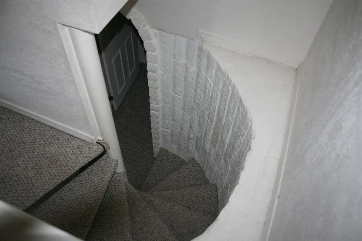 A narrow, carpeted spiral staircase curves downward into a white, brick-walled stairwell.