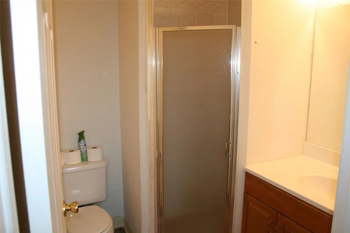 A small, neutral-toned bathroom featuring a toilet, a glass-enclosed shower, and a vanity with a white countertop.
