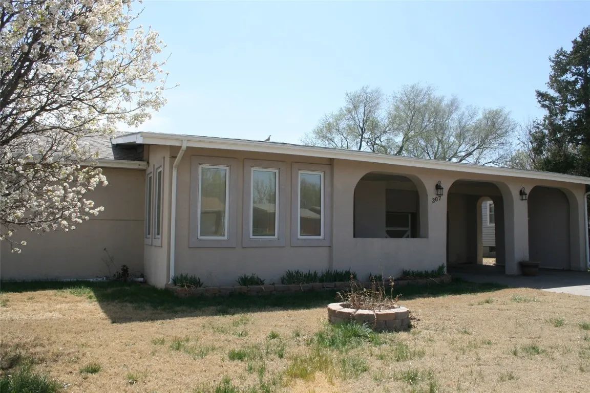 A single-story, beige stucco house with an arched front porch and a blooming tree in the front yard on a sunny day.