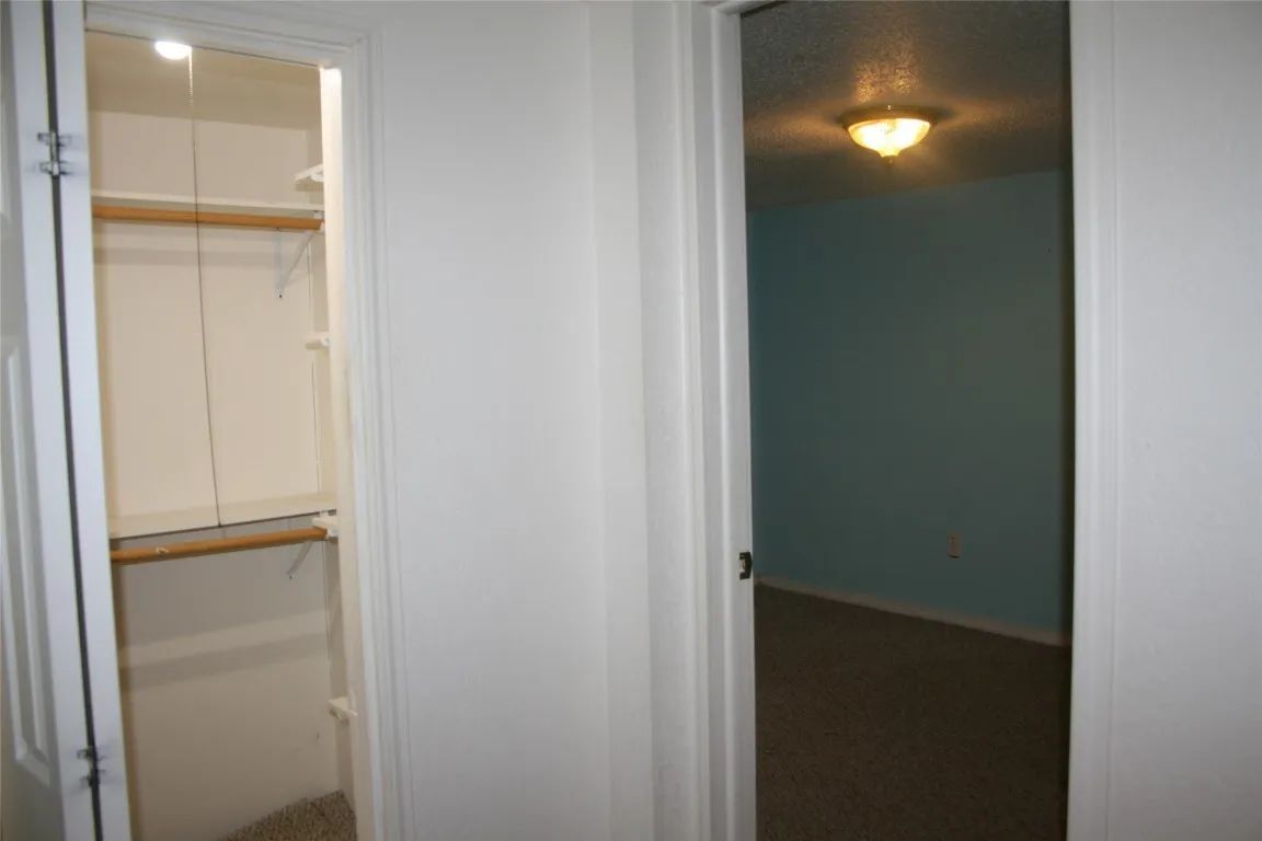 An open doorway revealing a closet with shelves and rods on the left, next to a doorway leading into a blue-walled room.