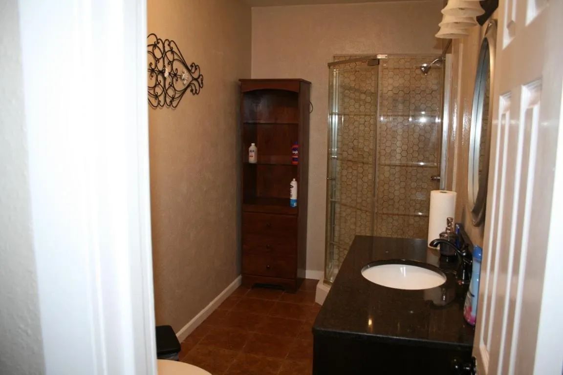 A bathroom with a dark vanity, sink, glass-enclosed shower, tall wooden cabinet, and tan walls.