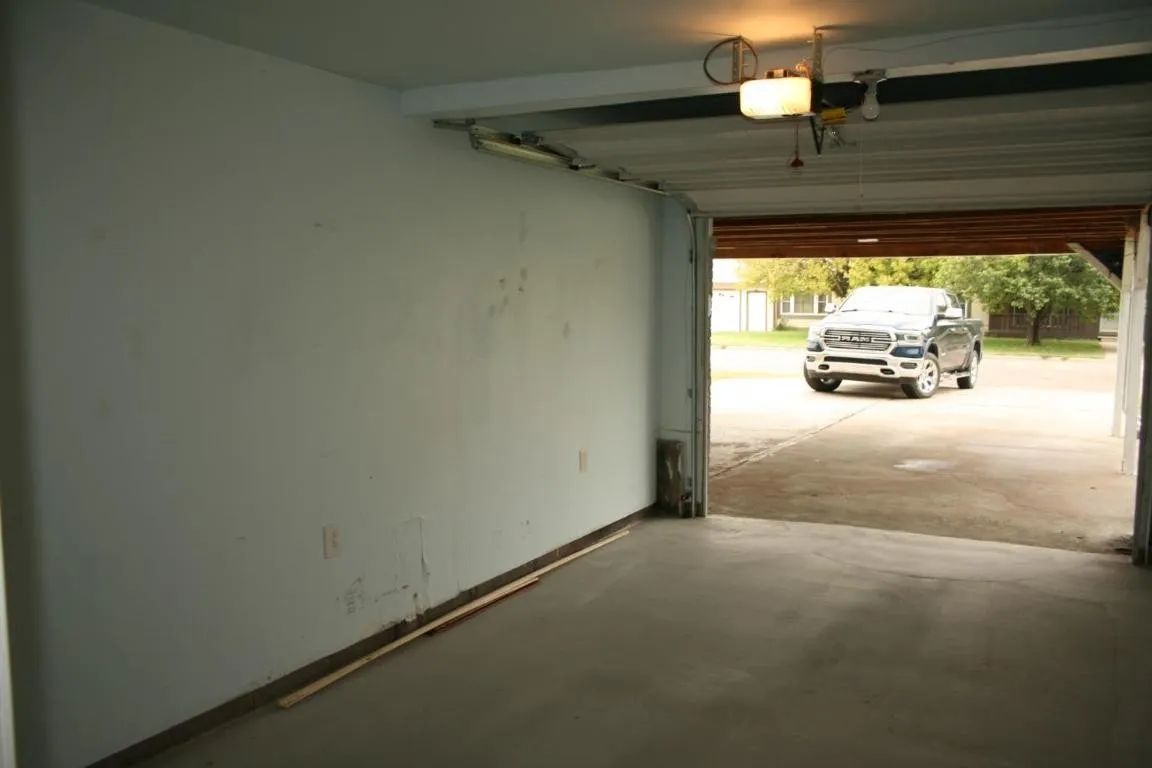 An empty garage with white walls and a concrete floor, looking out toward a parked pickup truck on a driveway.