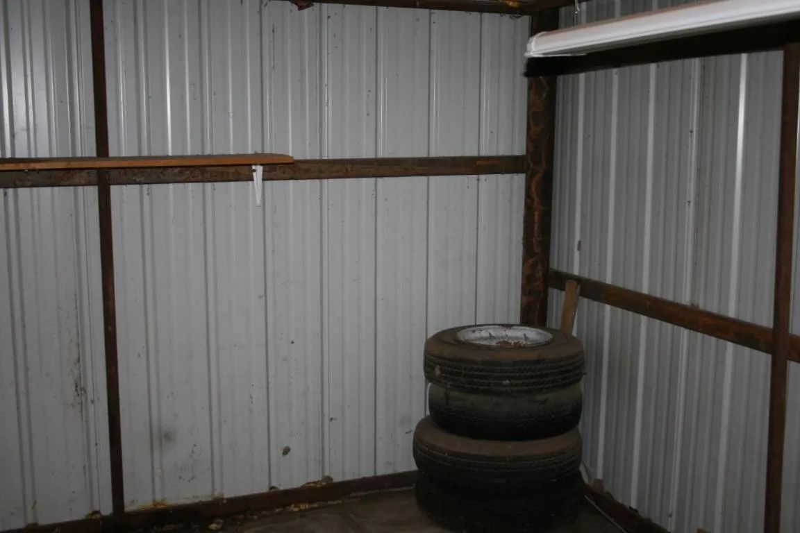 A stack of two tires sits in the corner of a shed with corrugated metal walls and wooden framing.
