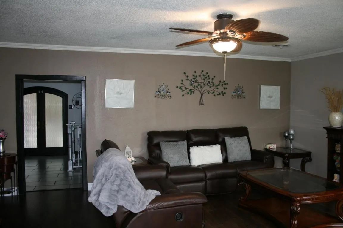 Living room with a brown leather couch, ceiling fan, wall art, and a doorway leading to a tiled entryway.