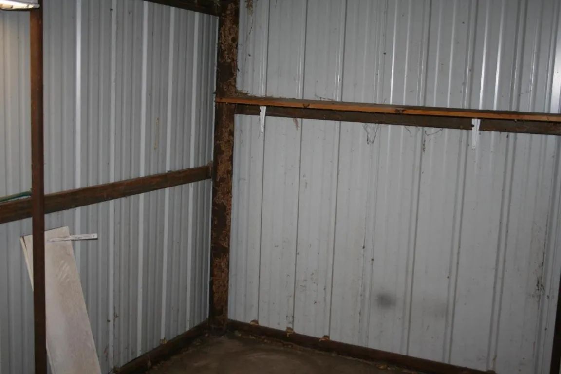 An indoor corner of a shed featuring white vertical corrugated metal walls and horizontal wooden support beams.