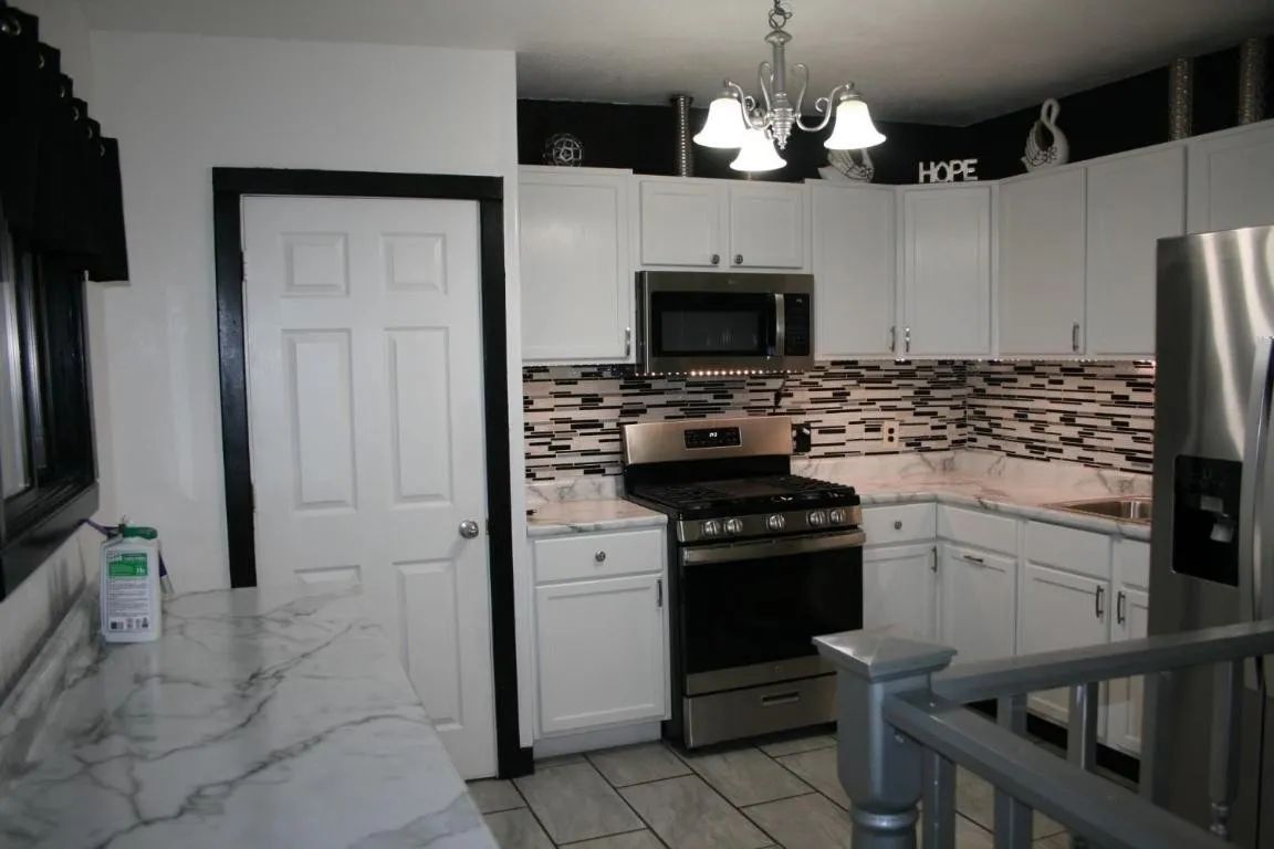 A kitchen with white cabinets, stainless steel appliances, a patterned tile backsplash, and black trim around a doorway.