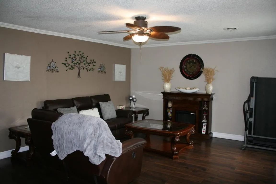 A living room with brown walls, a dark sofa, a wooden coffee table, a fireplace, and a ceiling fan.
