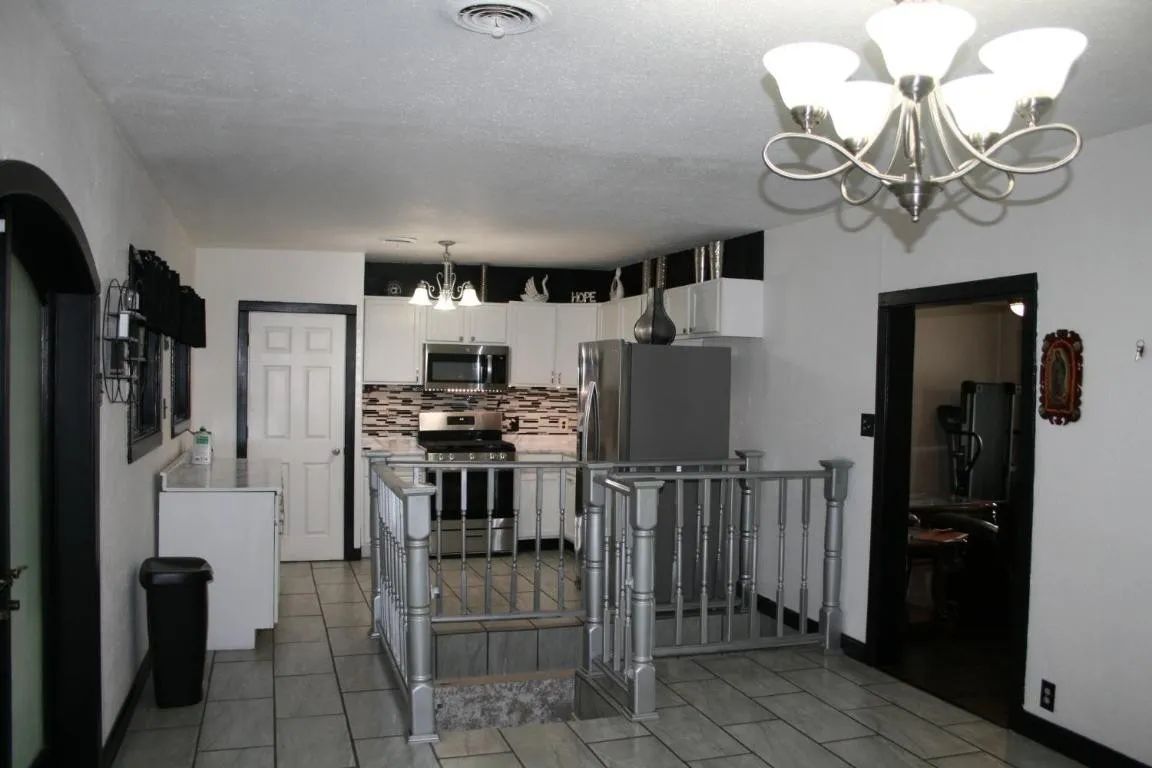 A kitchen with white cabinets, stainless steel appliances, and a gray-railed staircase leading to a lower level.