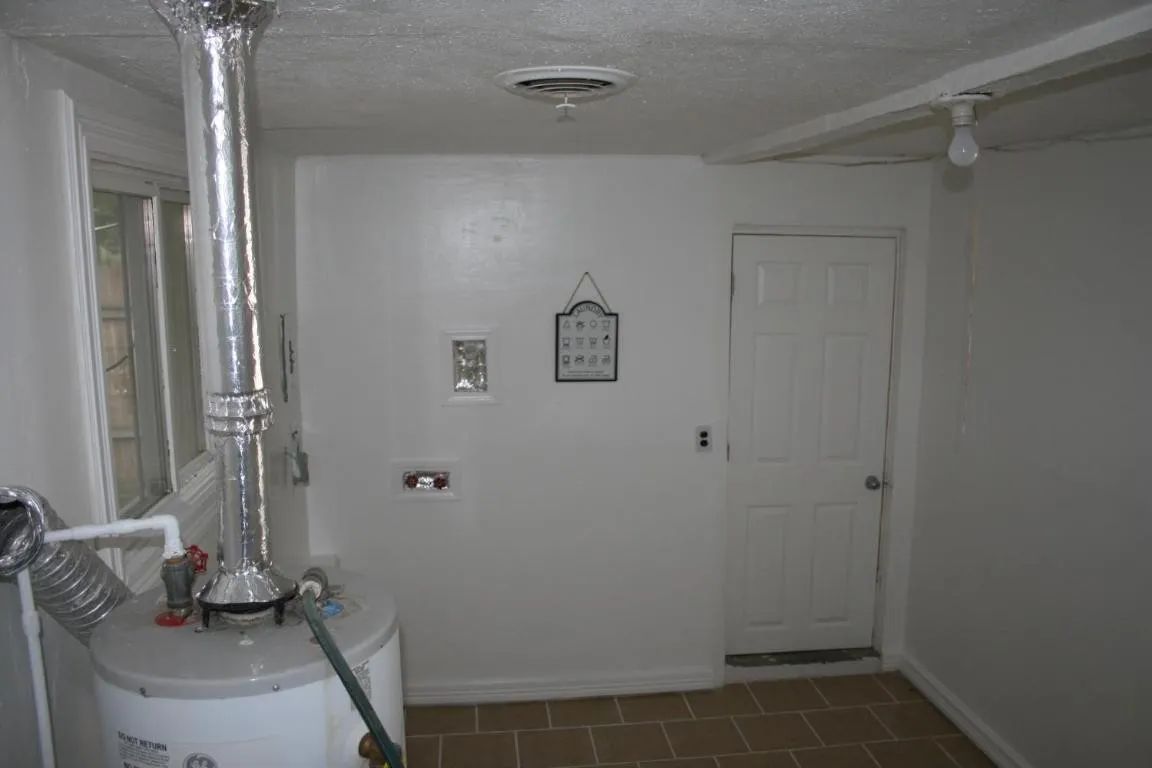 A utility room featuring a water heater with a vent pipe, a white door, and a small wall decoration on a white wall.